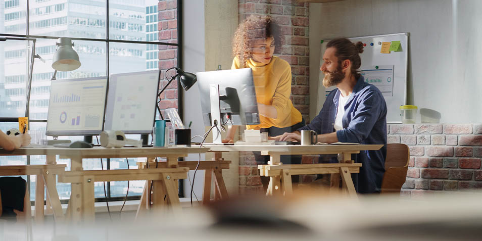 Two employees talking at their desks (Photo)