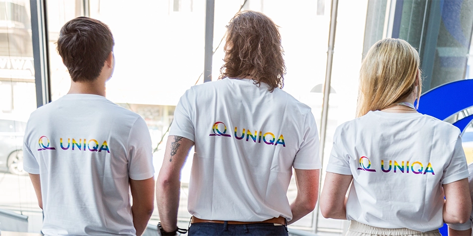 Back view of three young people wearing T-shirts with the UNIQA logo in rainbow colors.
