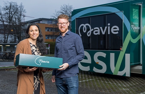 A man and a woman smiling while holding Mavie promotional materials.
