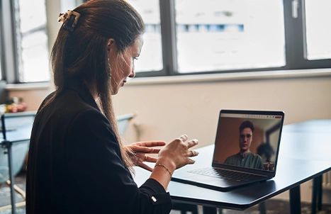 A woman and a man in a video call in an office setting.
